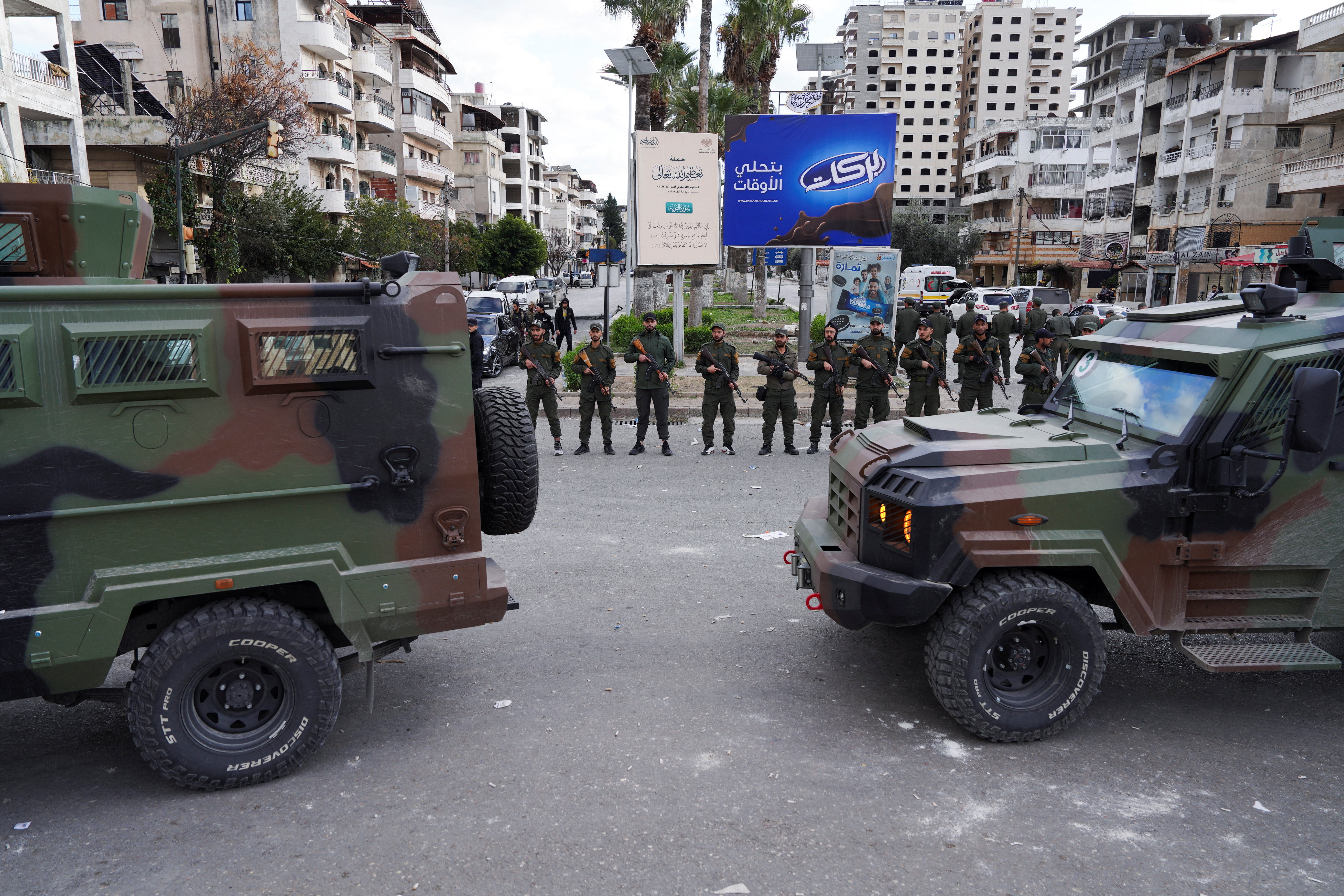 Members of the Syrian Security forces stand guard near military vehicles on the day people from the Alawite sect protest as they demand federalism and an end to what they say is the killing and violations against Alawites, in Latakia, Syria, December 28, 2025. REUTERS/Karam al-Masri