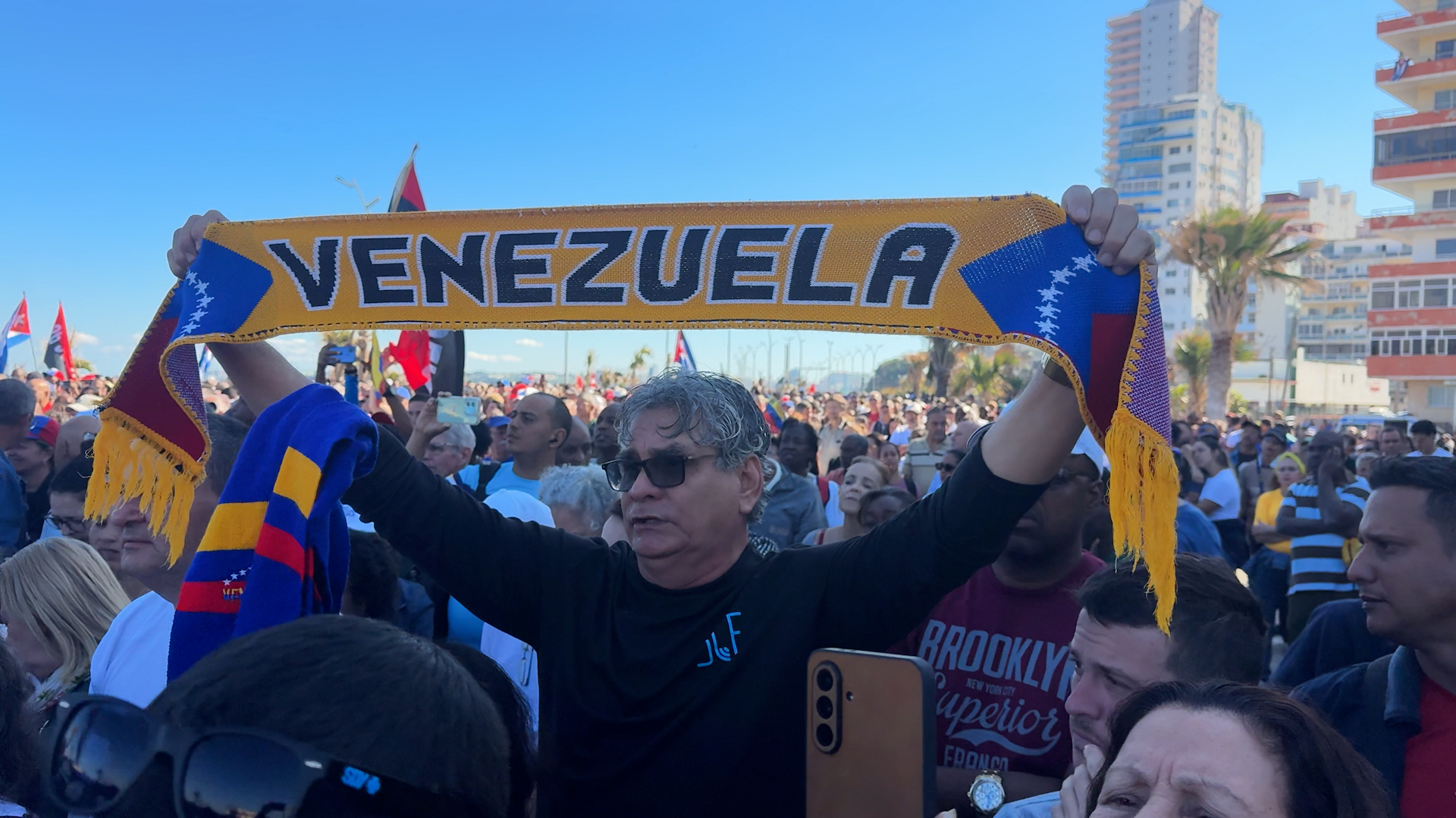 A man at a protest holds up a scarf that reads, "Venezuela"