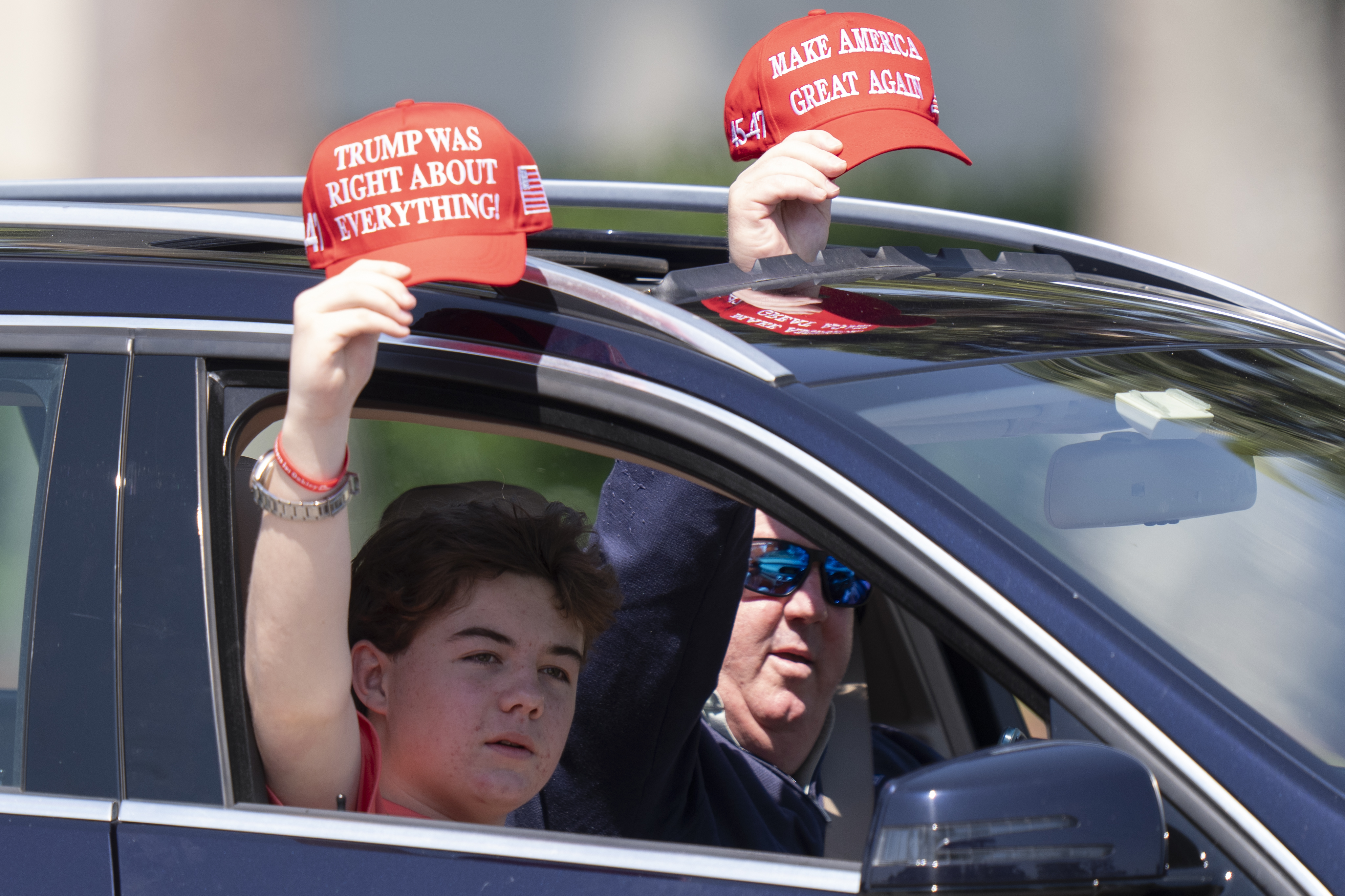 Trump supporters in a car hold up baseball caps that read, "Trump was right about everything."