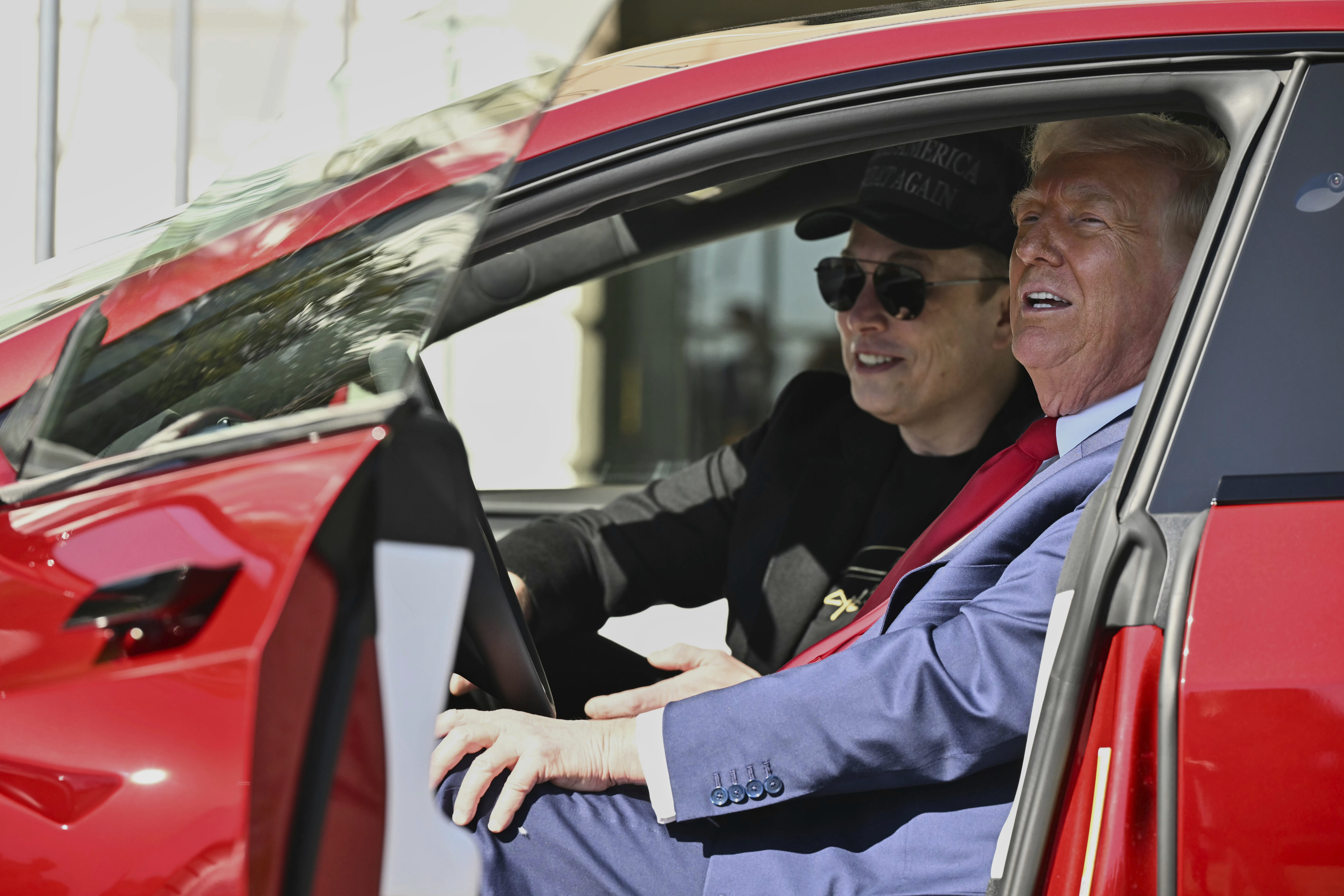 Donald Trump and Elon Musk pose in a red Tesla