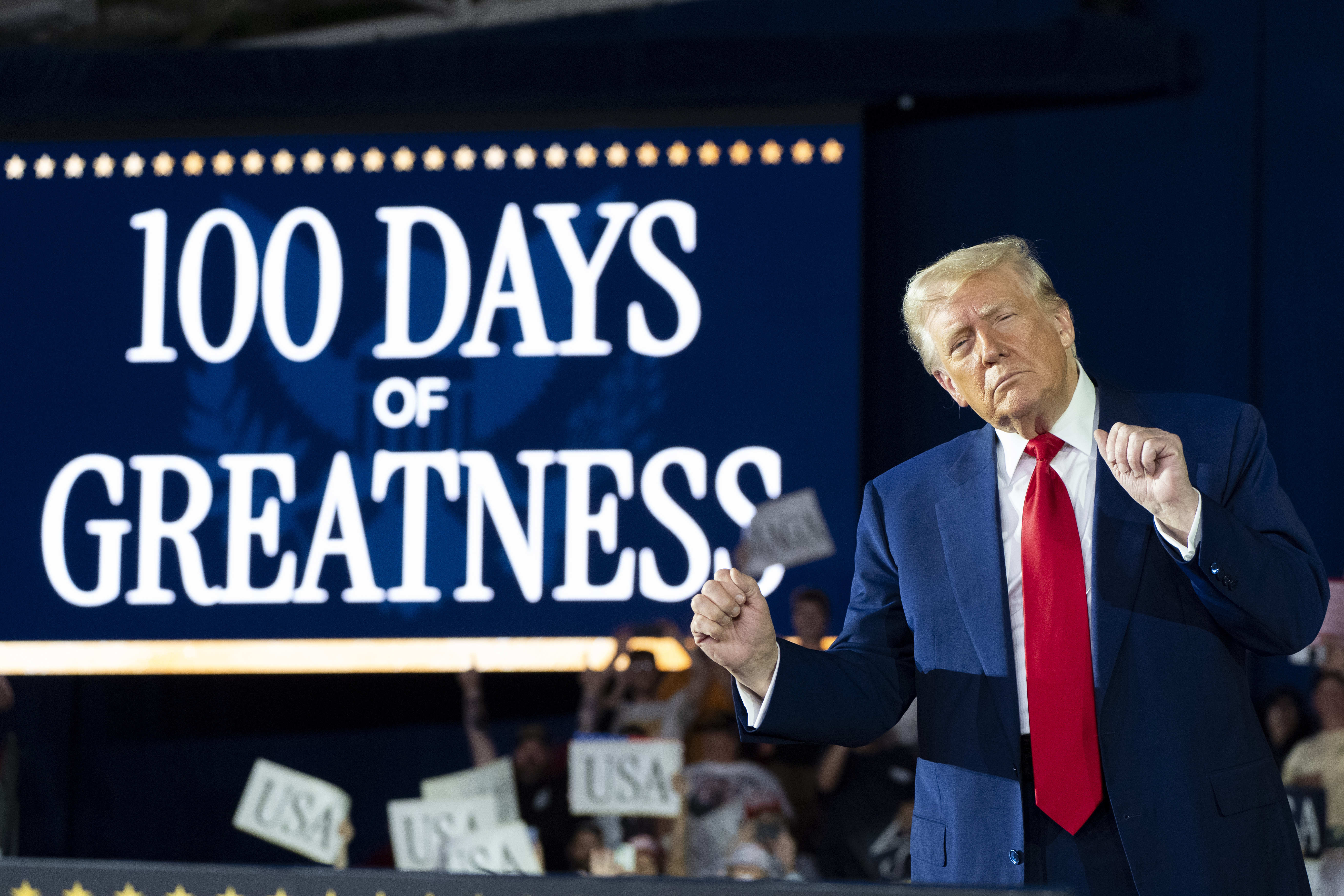 Trump speaks in front ofa a sign that reads "100 days of greatness"