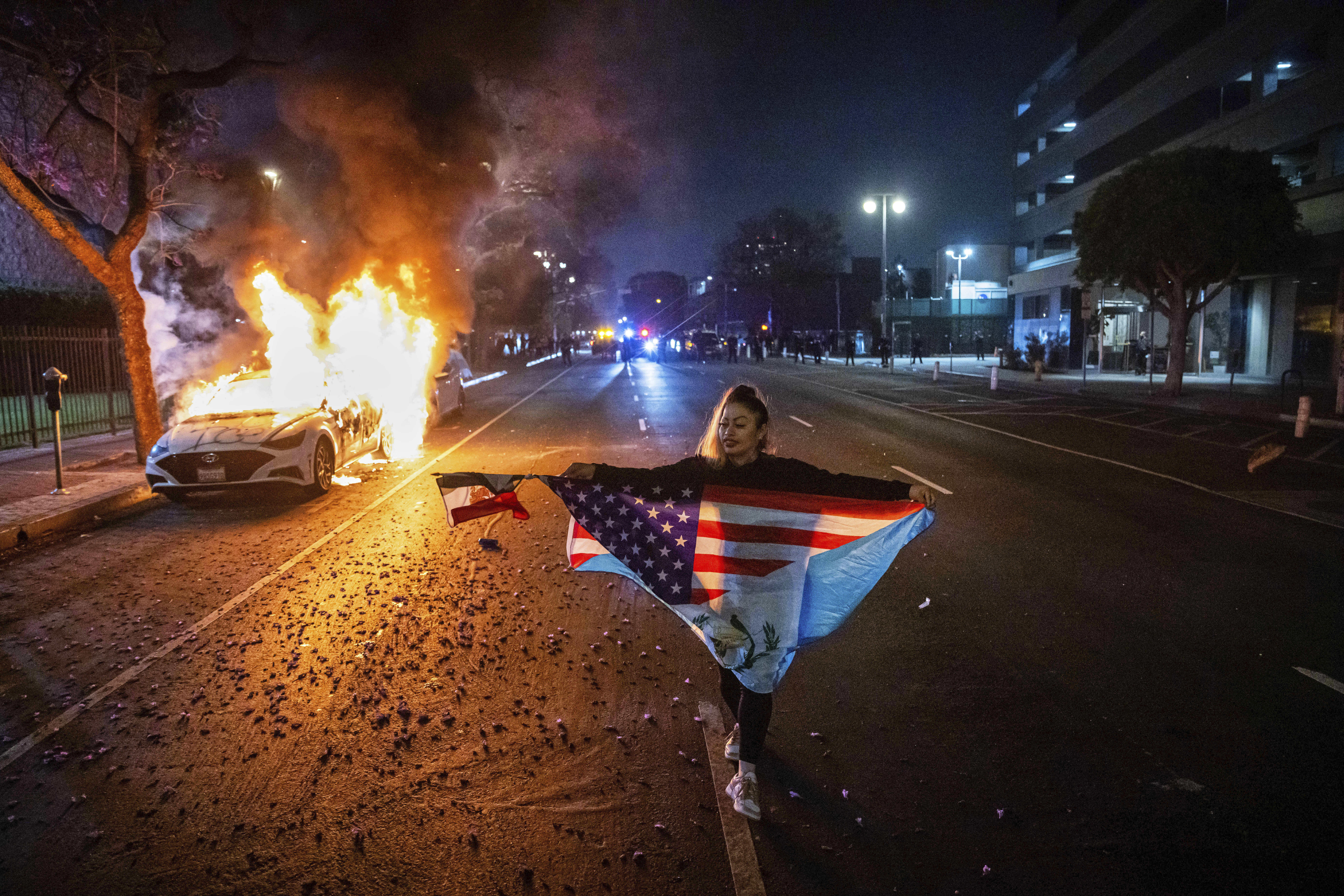 A protester holds up a flag as a car burns behind them