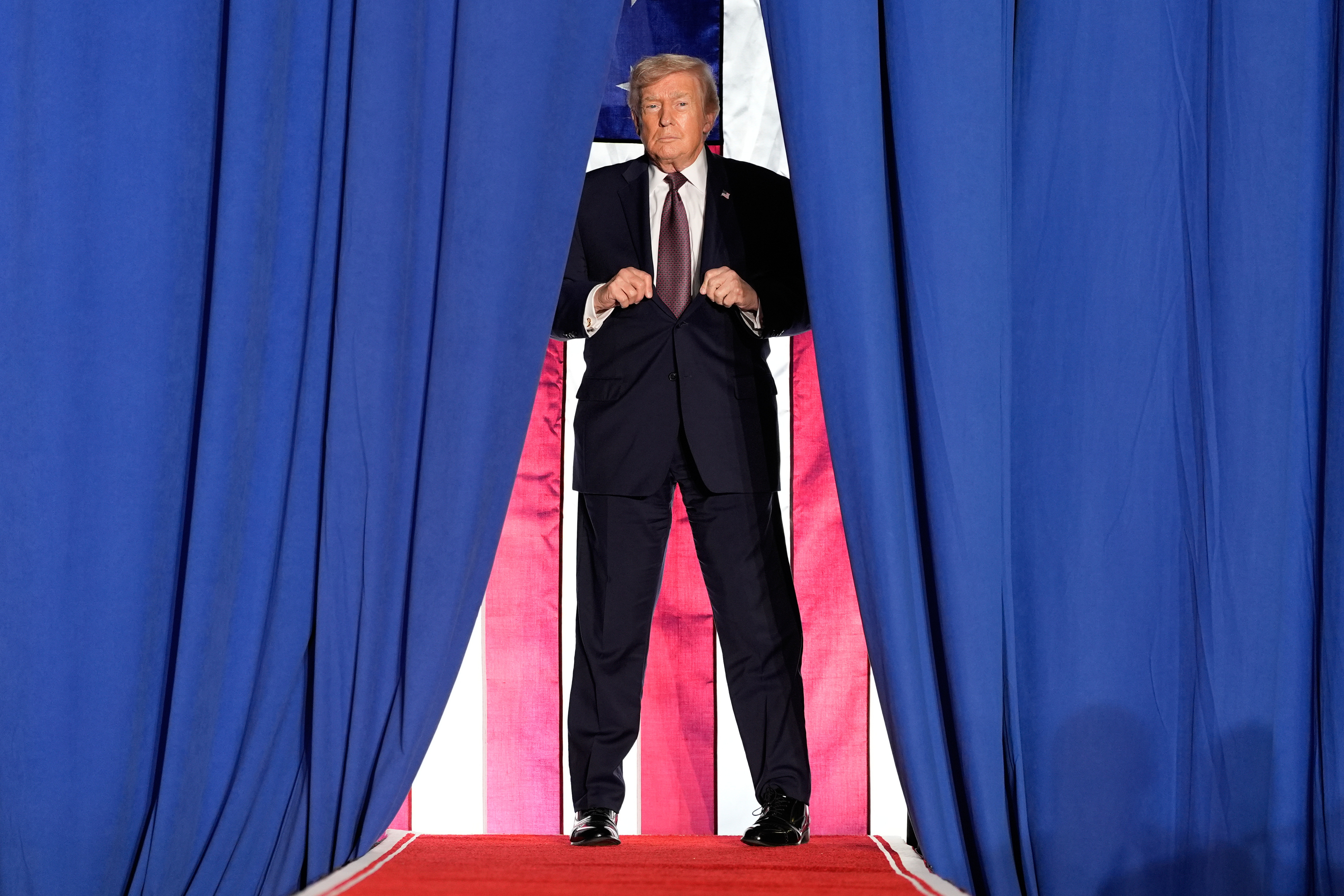 Trump appears on stage between two curtains.