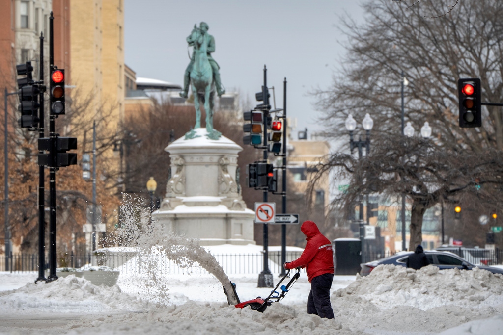 A man with a snowblower with a statue in the background