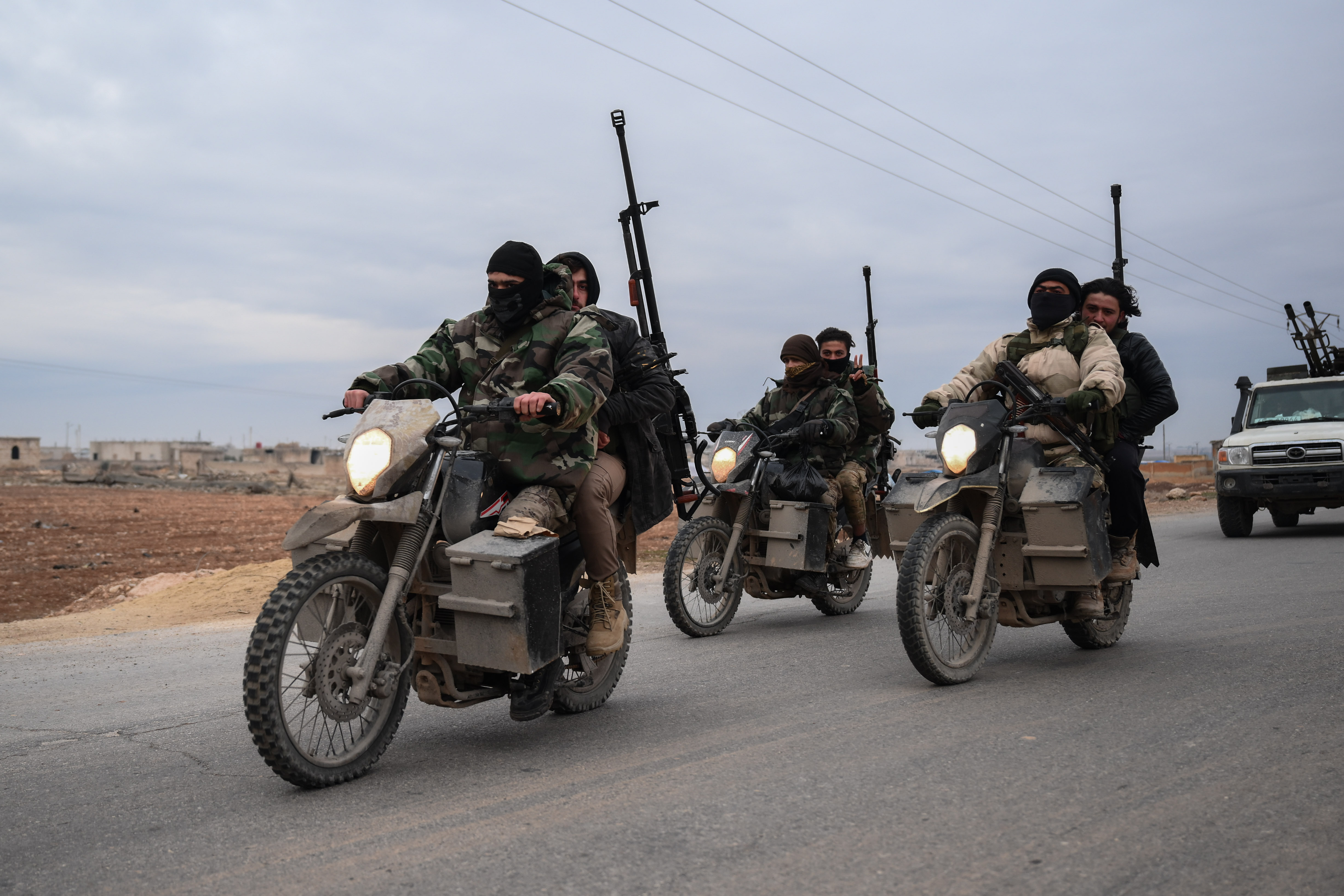 Syrian army forces drive on motorbikes in front of a military vehicle.