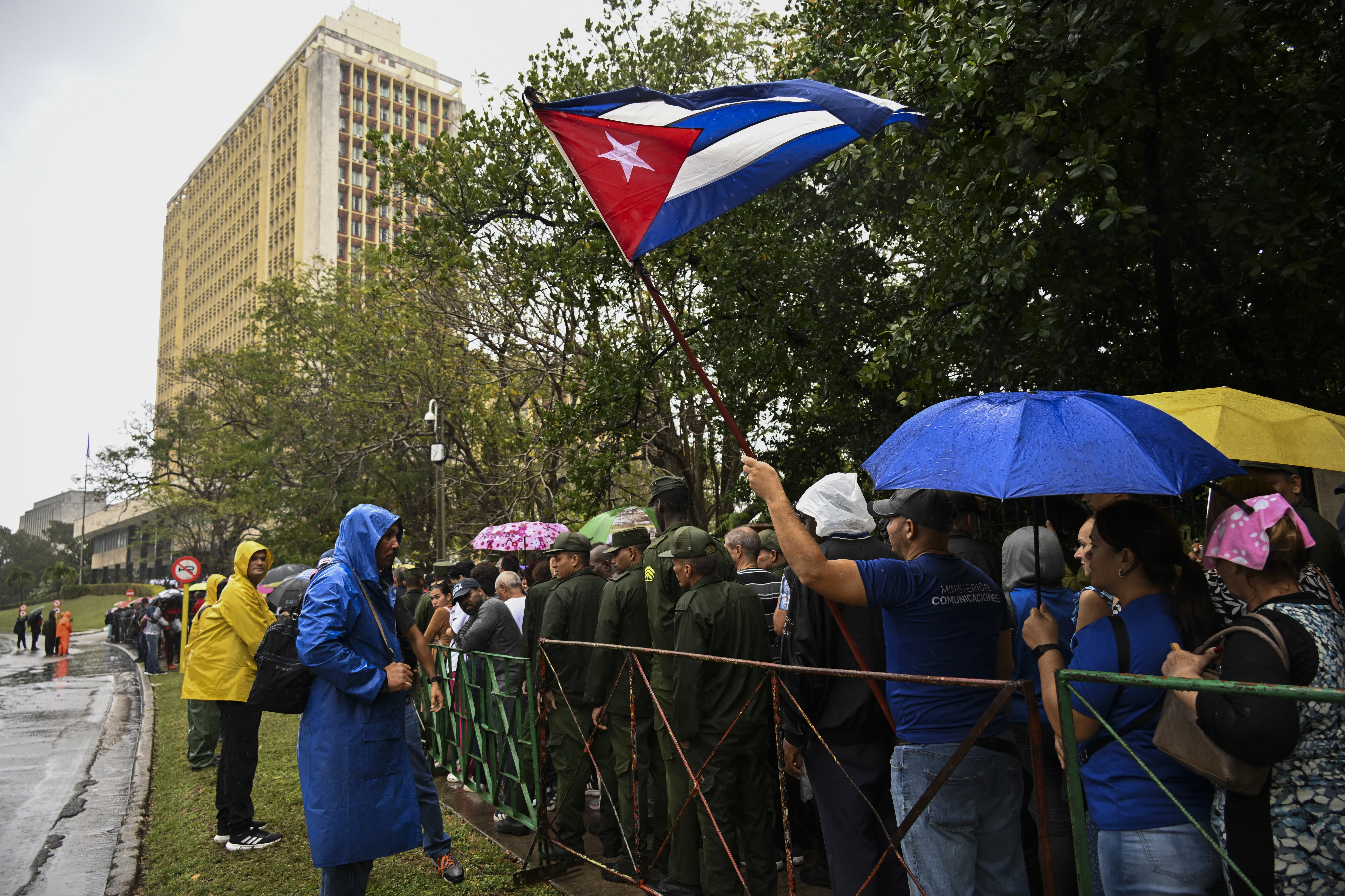 TOPSHOT - Cubans protect themselves from the rain wearing umbrellas as they queue outside the Ministry of the Revolutionary Armed Forces to pay their respects to the 32 Cuban soldiers who died during the US incursion to capture Venezuelan leader Nicolas Maduro, during the funeral honors in Havana on January 15, 2026.