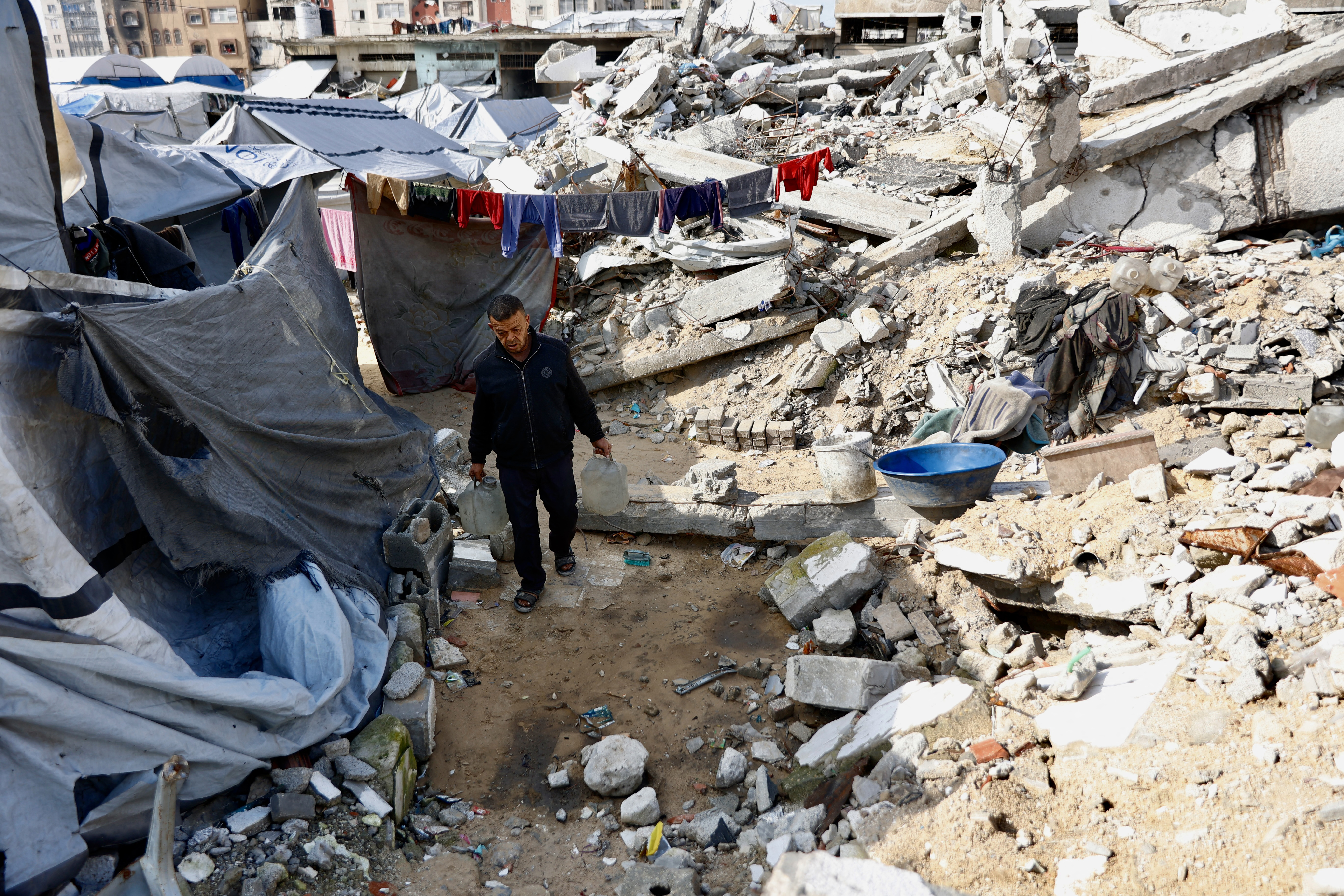 A man carries jerrycans past tents erected next to rubble in Gaza City on January 20, 2026.