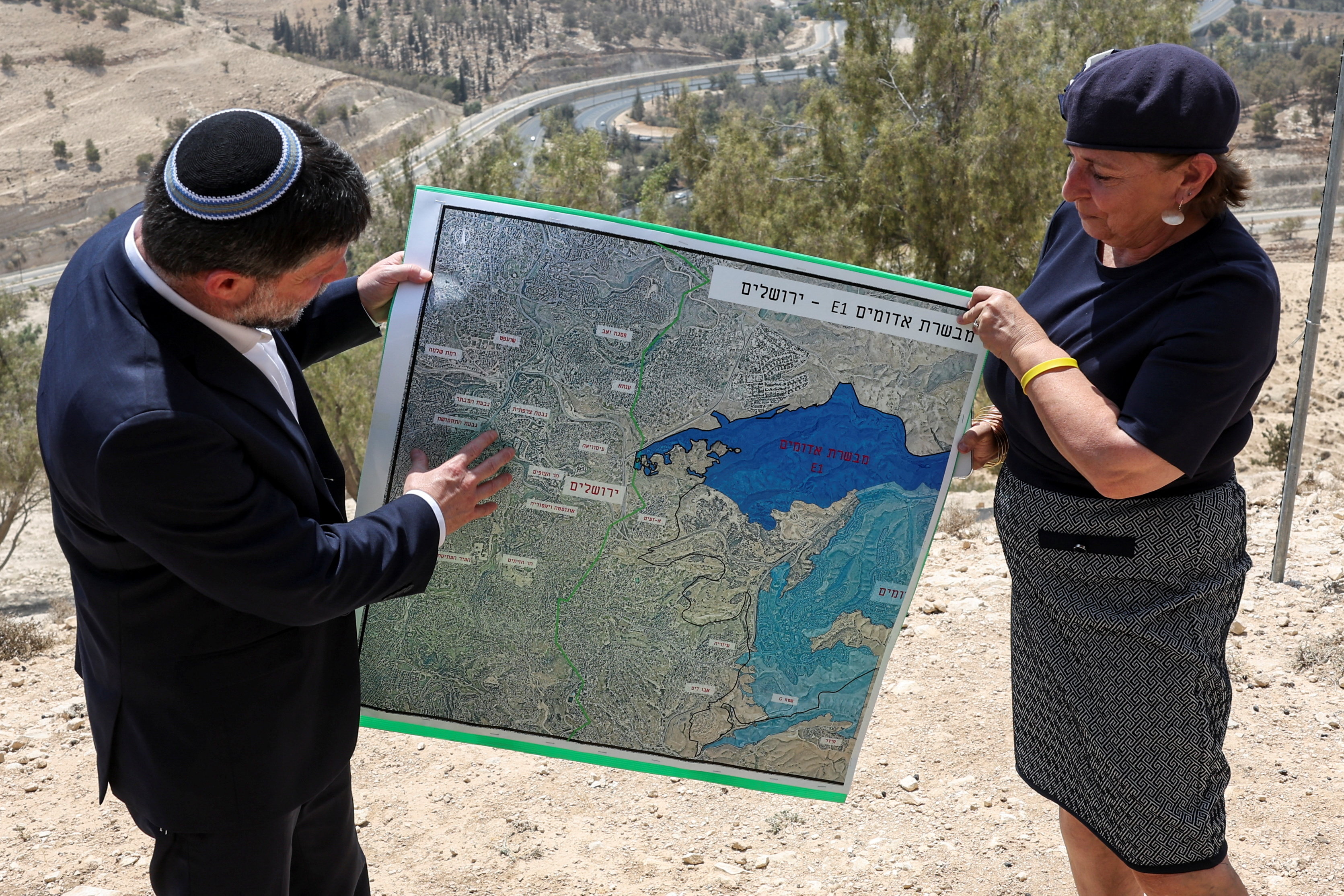 Israeli Finance Minister Bezalel Smotrich and a woman hold up a map that shows the long-frozen E1 settlement scheme, which would split occupied East Jerusalem from the occupied West Bank, near the illegal Israeli settlement of Maale Adumim