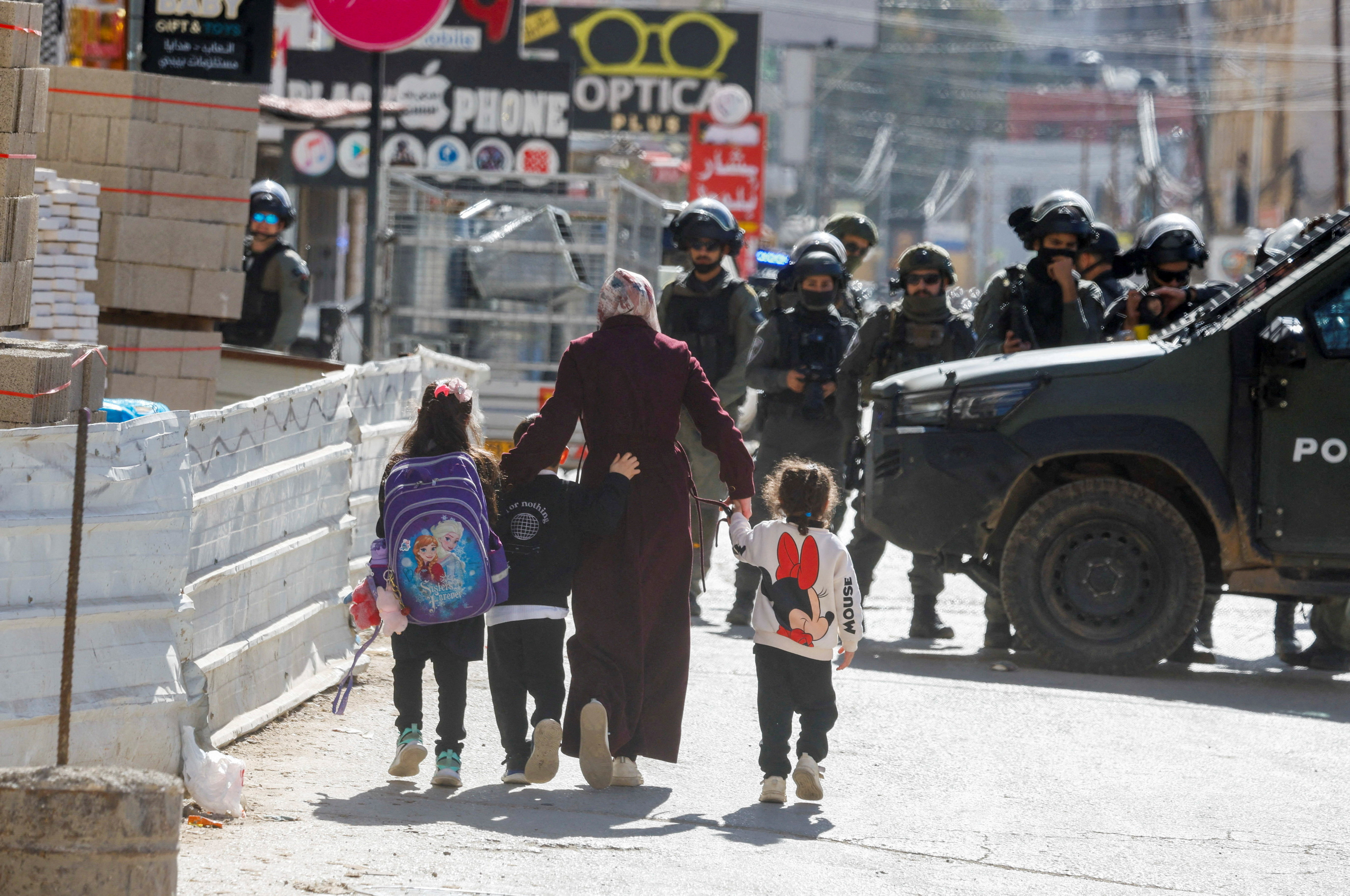 A Palestinian woman with children walks near members of Israeli border police during an Israeli raid in Qalandya, in the Israeli-occupied West Bank, January 26, 2026. REUTERS/Mohamad Torokman TPX IMAGES OF THE DAY
