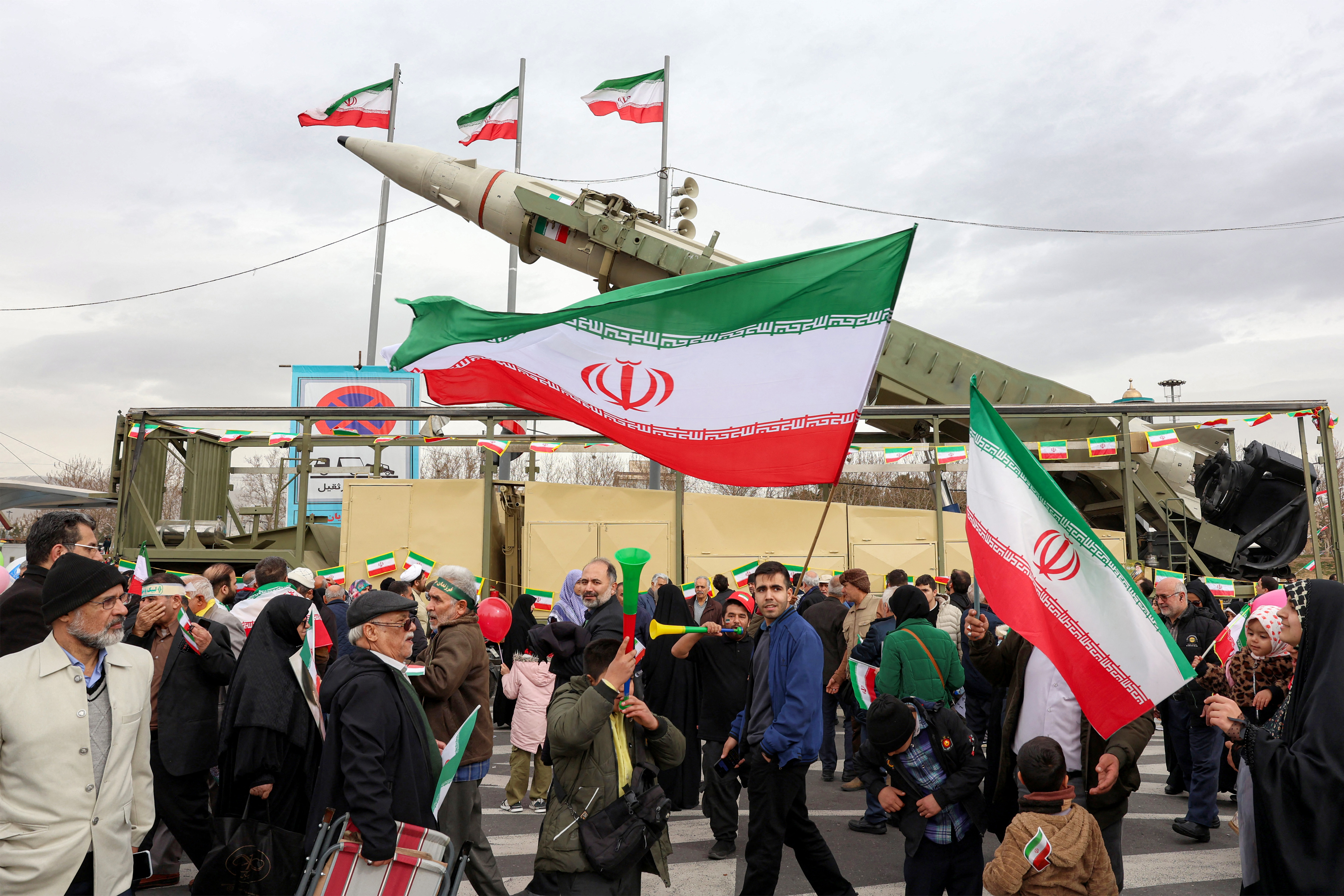 People walk with Iranian national flags near a ballistic missile launch vehicle in Tehran on February 11, 2026, during a rally marking the 47th anniversary of the 1979 Islamic revolution. The Persian calendar date of Bahman 22 celebrates the anniversary of the resignation of the ousted shah's last prime minister and the formal assumption of power by revolutionary leader Ayatollah Ruhollah Khomeini. (Photo by AFP)