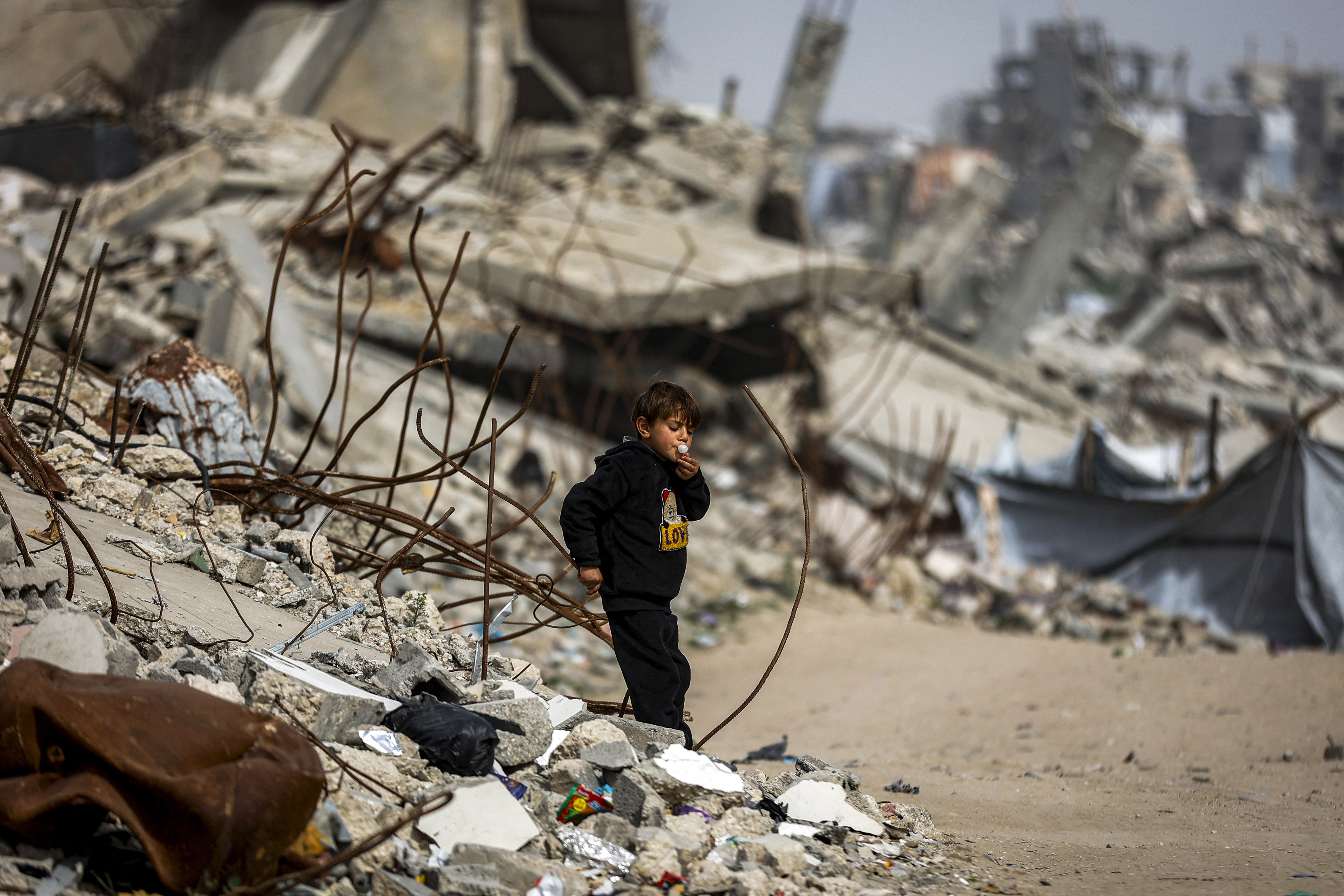 A boy blows a bubblegum while walking past destroyed buildings in the Jabalia camp for Palestinian refugees in the northern Gaza Strip on February 8, 2026.