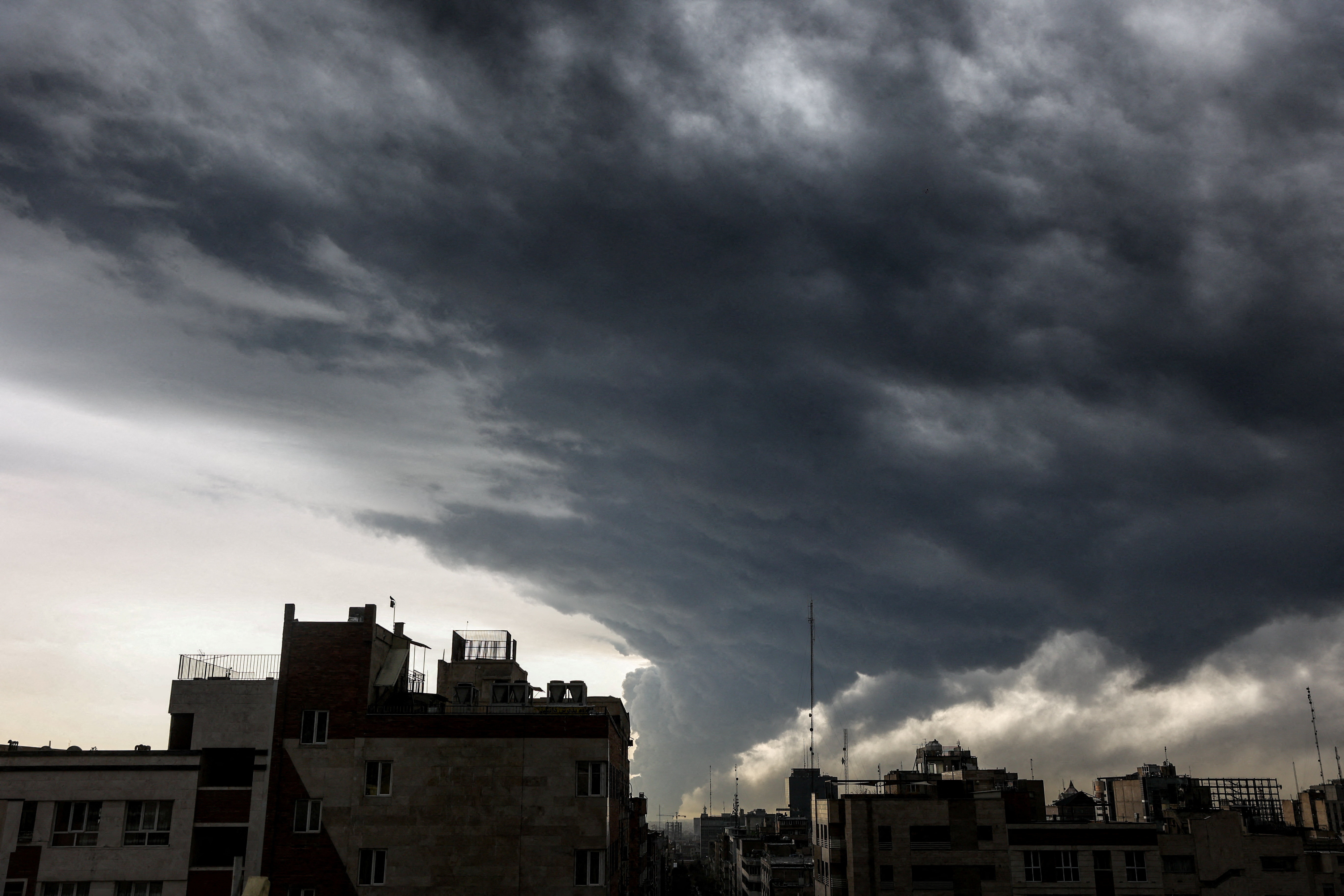 Plumes of smoke from an oil facility linger and merge with the cloudy sky over Tehran