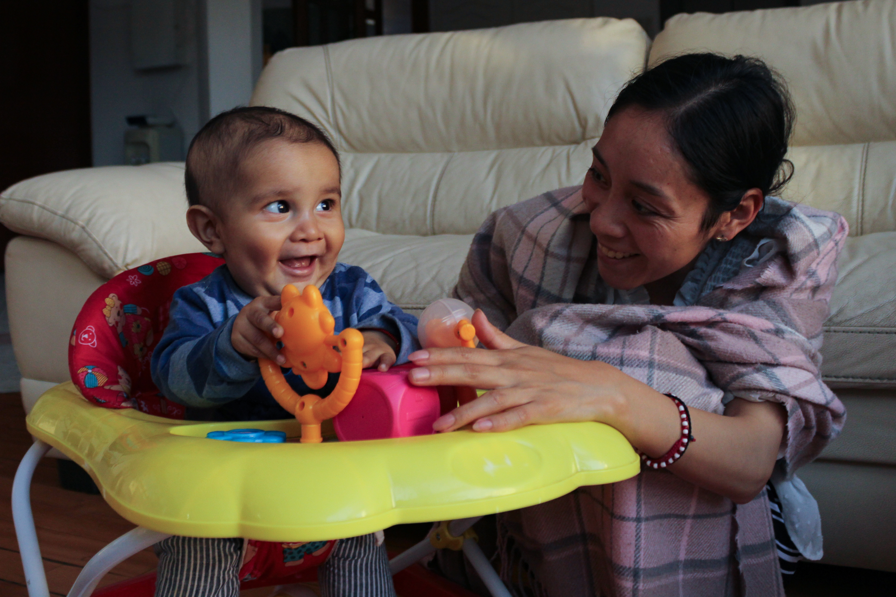 Seated in a play chair, Juan de Jesús laughs as he spins a small twirly toy, while his mother, Luisa, smiles beside him_-1773831295