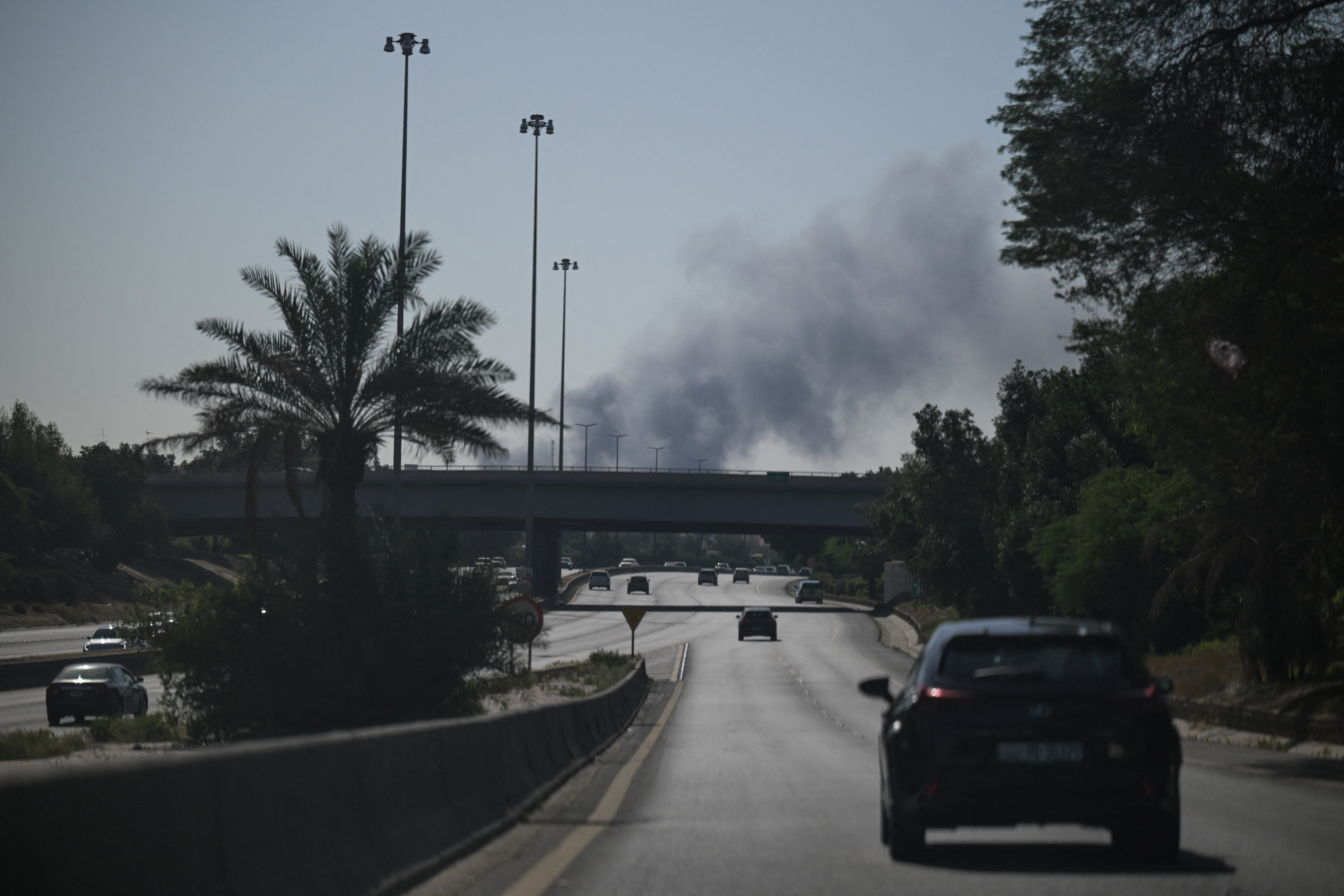 Motorists drive along a street as smoke rises from a reported Iranian attack in the area where the US Embassy is located in Kuwait City