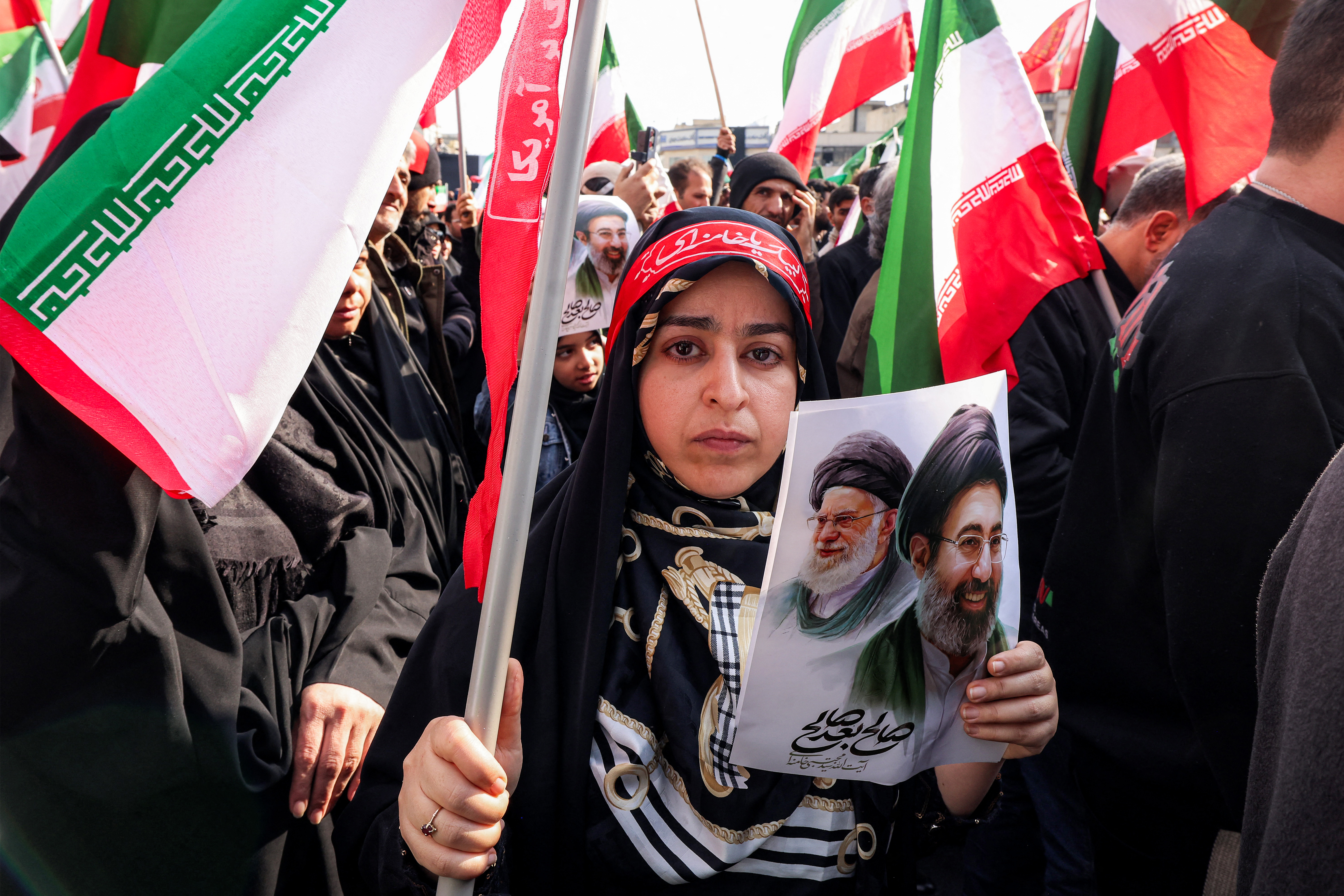 TOPSHOT - A woman holds a picture of Iran's new Supreme Leader Ayatollah Mojtaba Khamenei (R), next to his late father Ali Khamenei, during a rally in support of him at Enghelab Square in central Tehran on March 9, 2026.