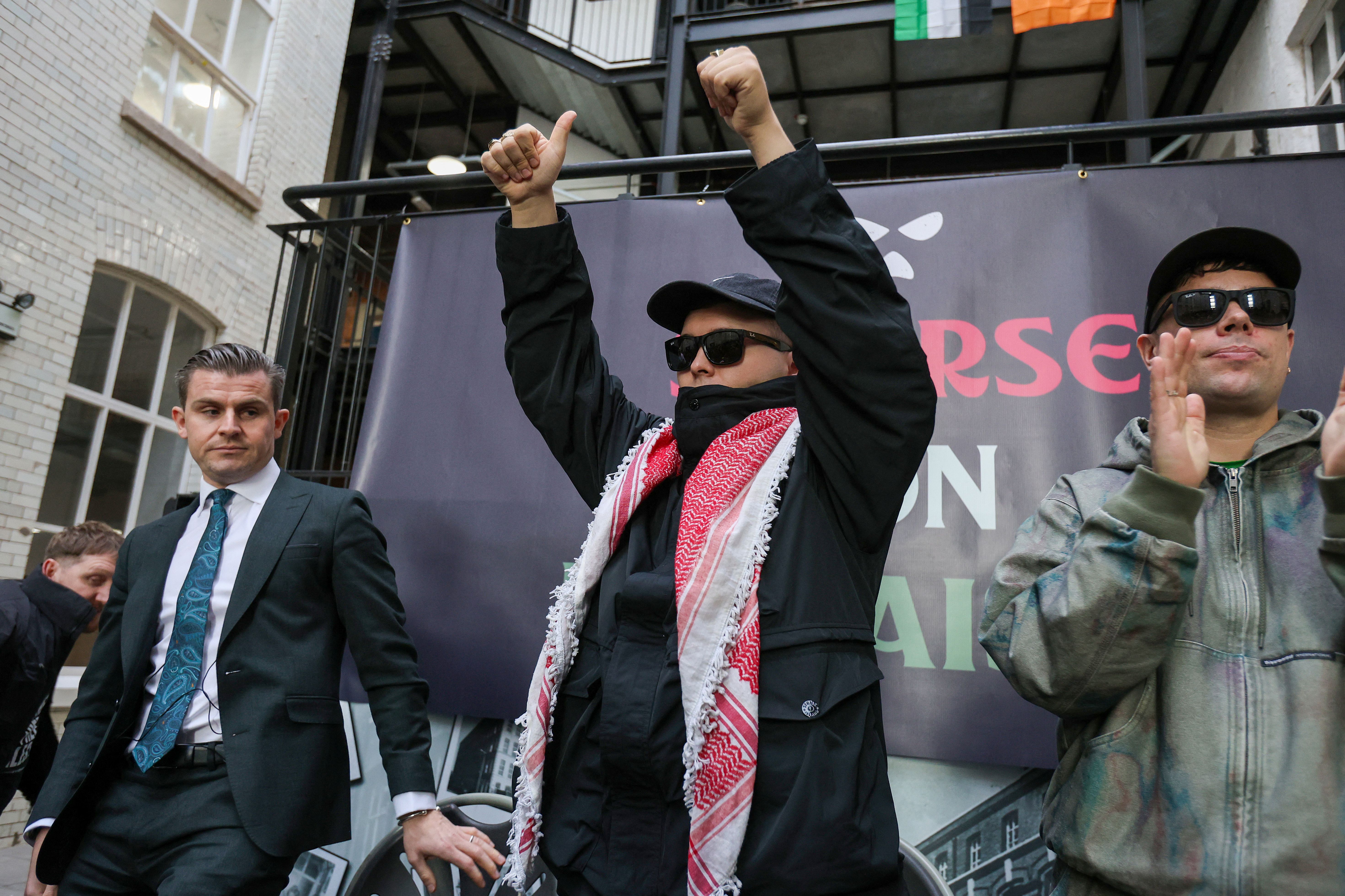 Liam O'Hanna (C), who performs under the stage name Mo Chara with punk-rap group Kneecap, attends a press conference with bandmate Naoise Ó Cairealláin (R), known as Moglai Bap, and Belfast-based lawyer Darragh Mackin (L) at the Conway Mill in Belfast on March 11, 2026.