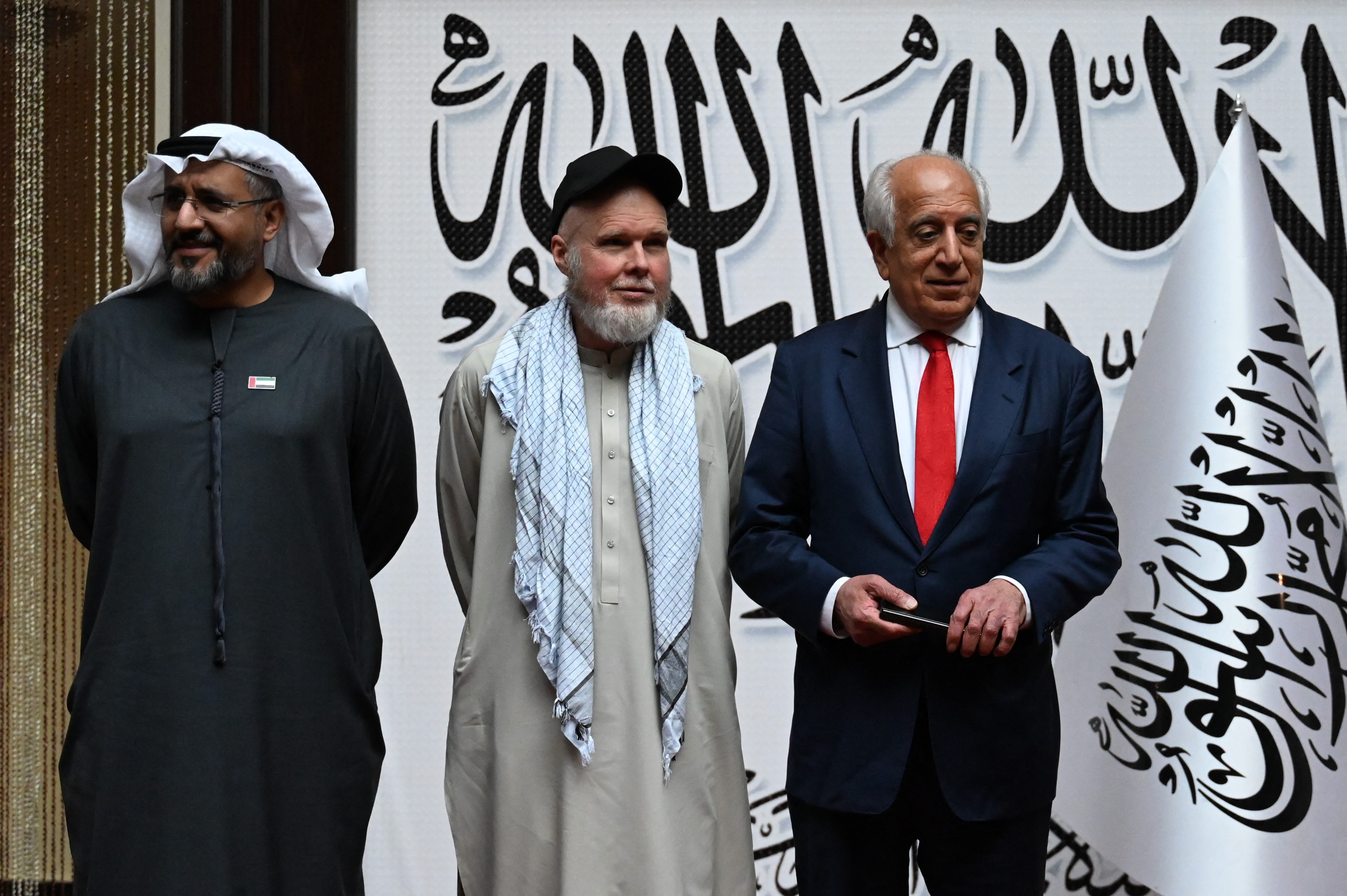 US citizen Dennis Coyle (C) upon his release by the Taliban, poses with US former special envoy to Afghanistan Zalmay Khalilzad (R) and the UAE ambassador to Kabul Saif Mohammed Al-Ketbi (L) at the airport in Kabul on March 24, 2026.