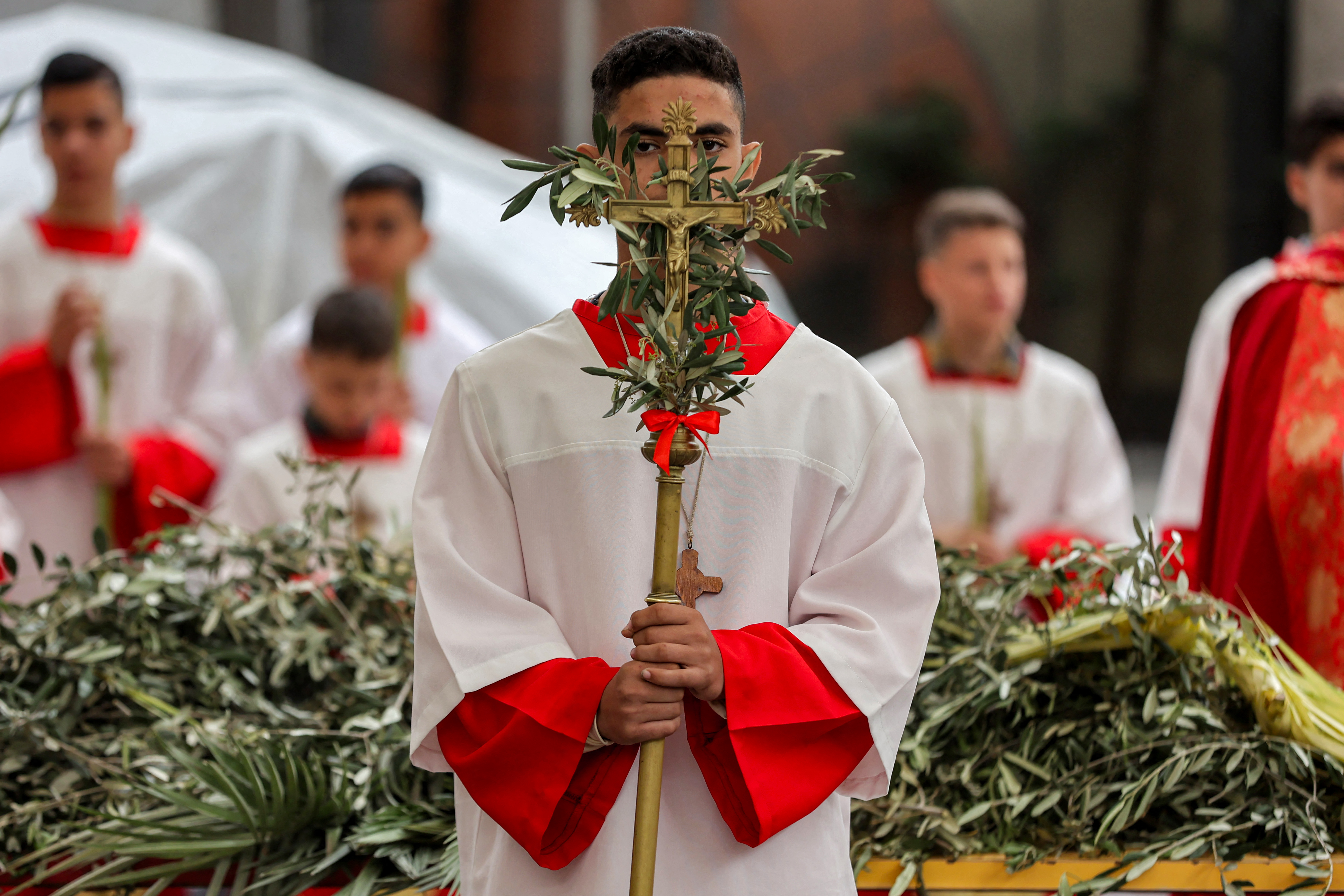 TOPSHOT - An altar server stands with a crucifix adorned with olive branches during the Palm Sunday service at the Roman Catholic Church of the Holy Family in Gaza City on March 29, 2026.