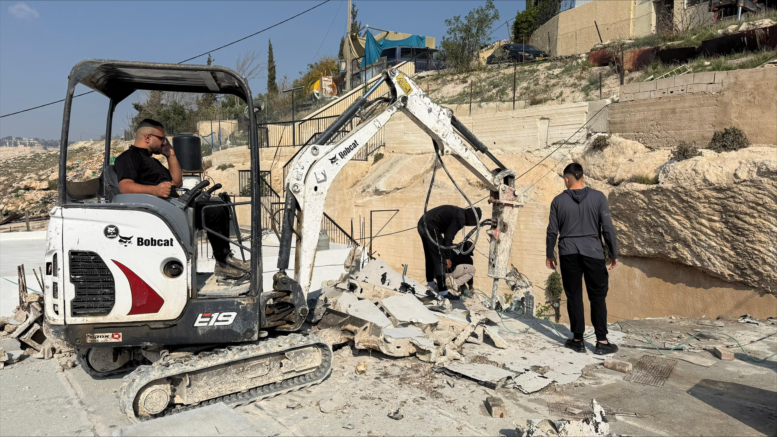 Bulldozer demolishing house as man stands nearby
