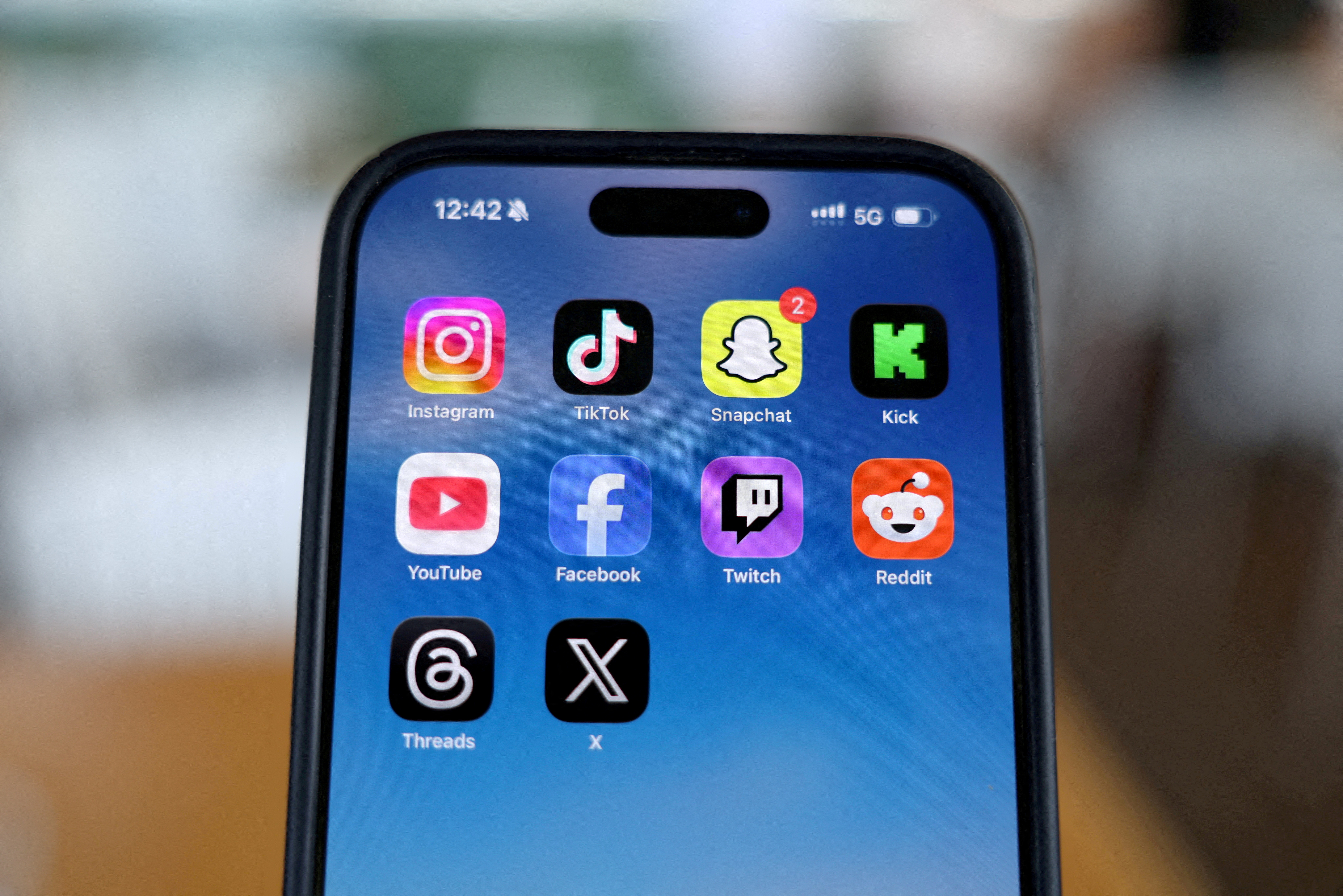 Instagram, TikTok, Snapchat, Kick, YouTube, Facebook, Twitch, Reddit, Threads and X applications are displayed on a mobile phone.