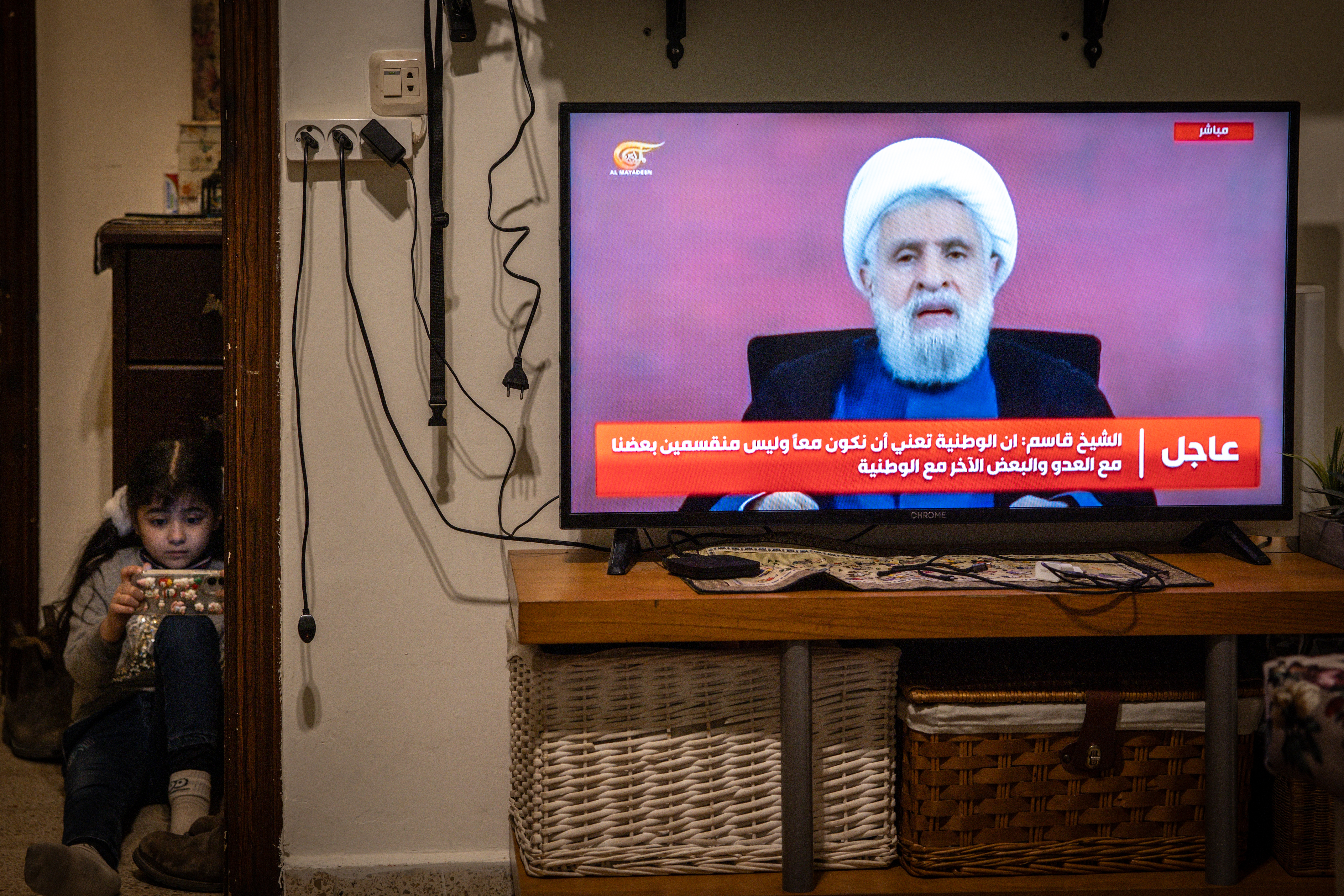 A young girl plays with a mobile phone as Hezbollah’s secretary-general, Lebanese Shia cleric, Naim Qassem appears on TV to address supporters on April 13, 2026, in Beirut, Lebanon.