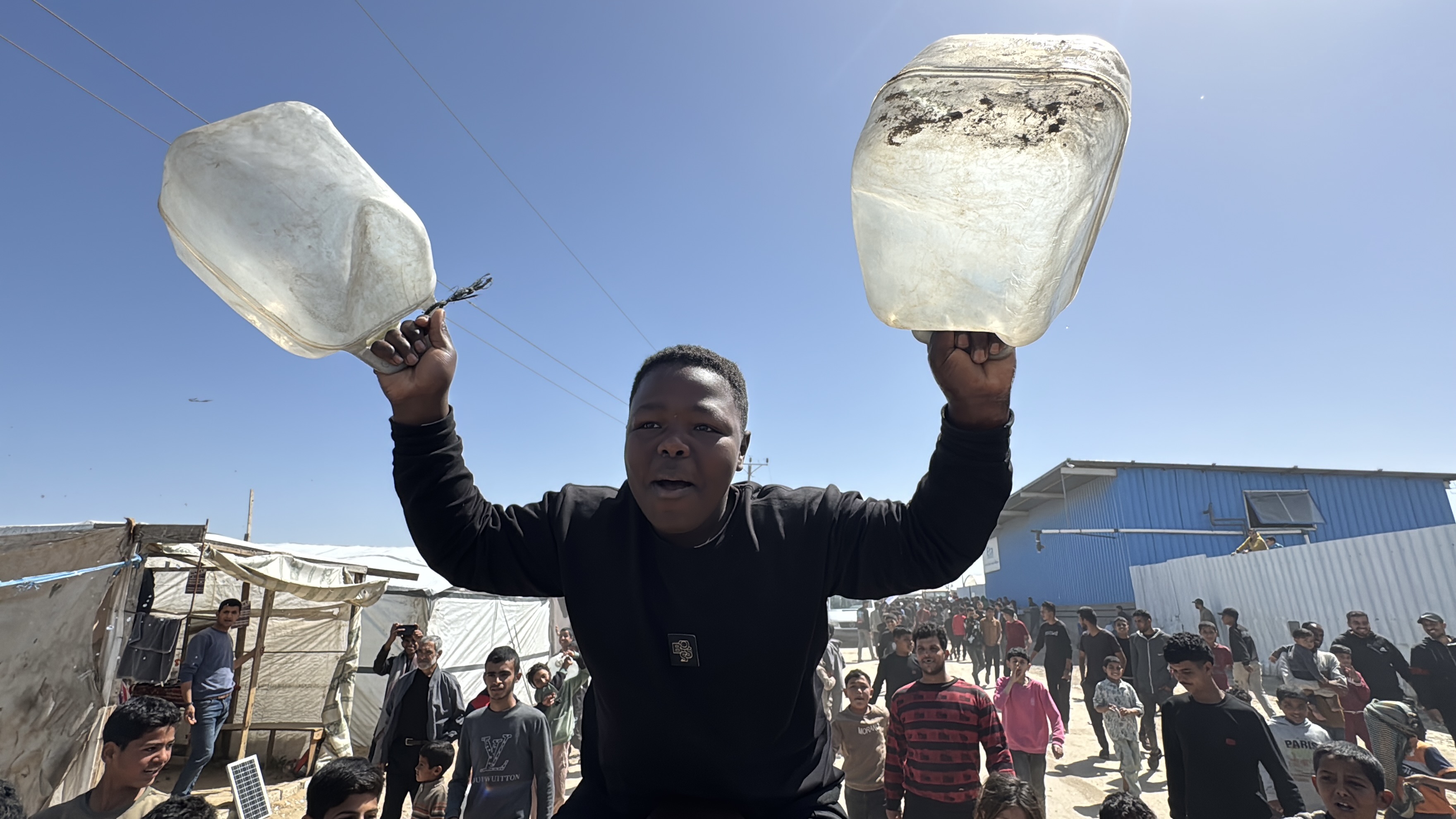 Child holds up empty jerry cans